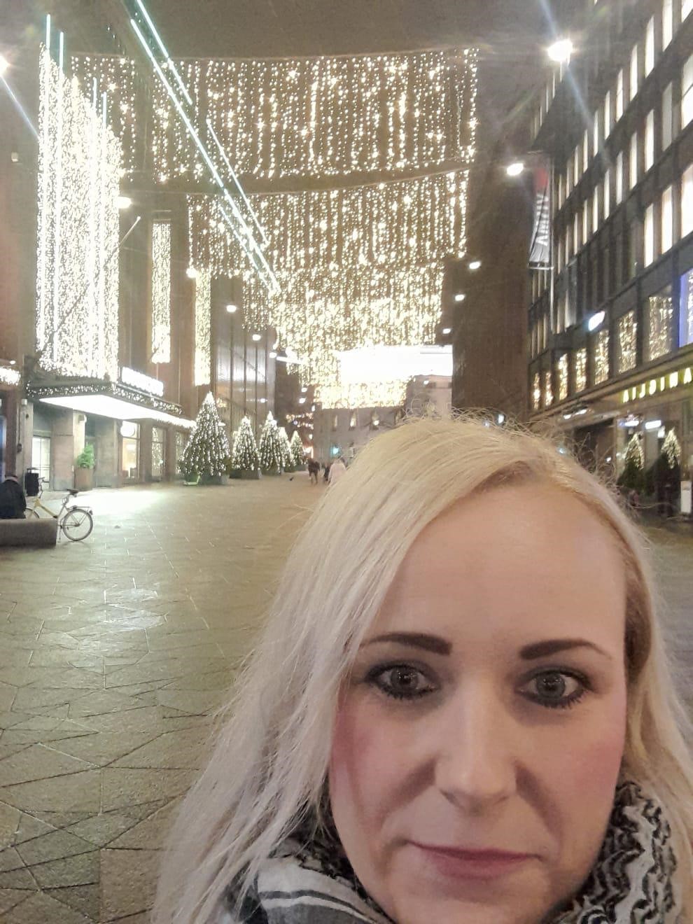 Kuraattorin selfie, jossa taustalla näkymä jouluisen Helsingin kadulle. 