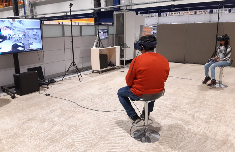 In this image number three we can see two students, one male and one female,  sitting on chairs and having virtual glasses on their heads. In front of them there are screens where some virtual reality model is being shown. 