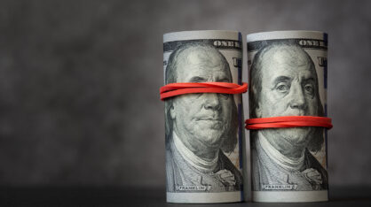 Rolls of hundred-dollar bills with red rubber bands on them, covering the mouth and eyes of Franklin's image.