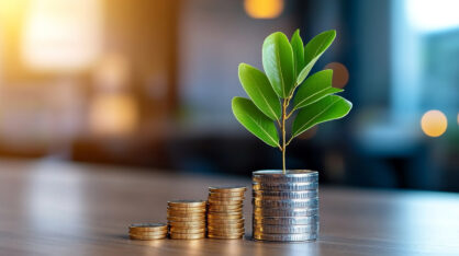 A pile of coins, and on top of one coin pile grows a plant.