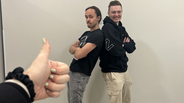 Podcastin puhujat Jimi ja Samu seisovat selät vastakkain ja poseeraavat, etualalla naisen käsi näyttää peukkua.