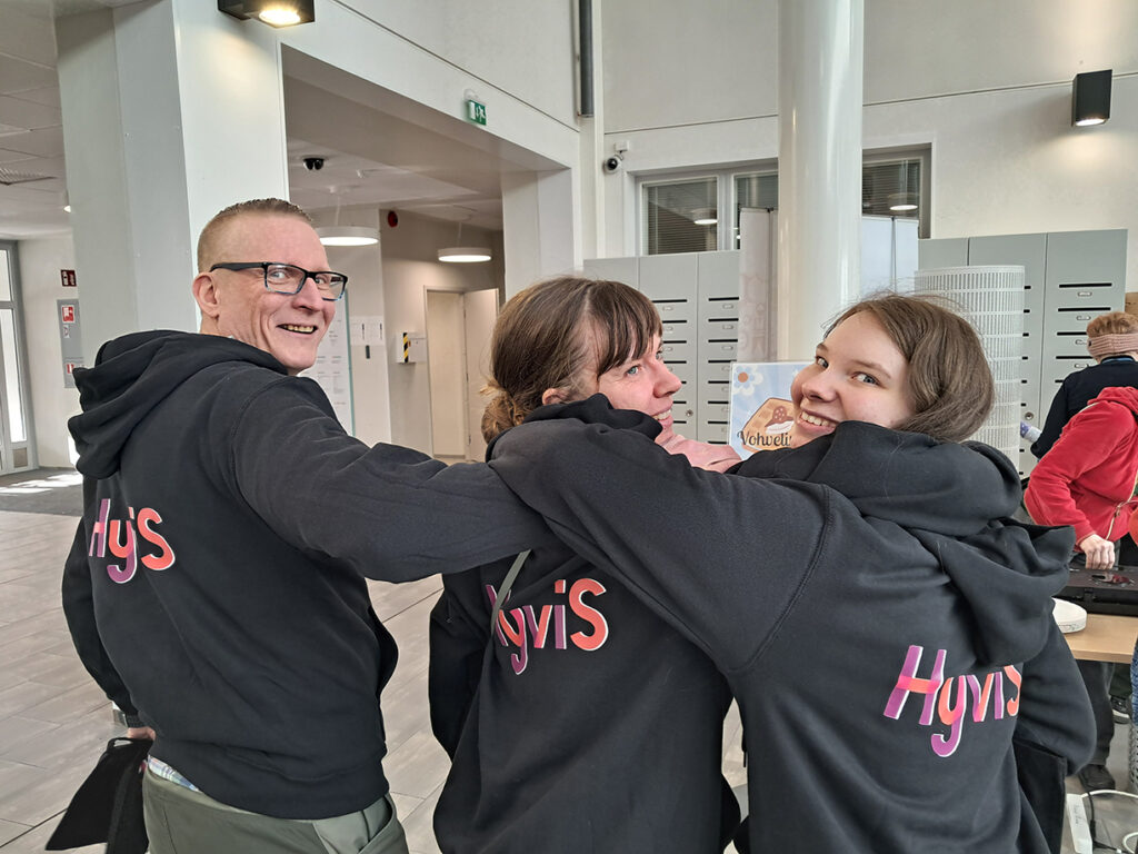 Opiskelijoita poseeraamassa mustat hupparit päällä, joiden selässä lukee HyviS
