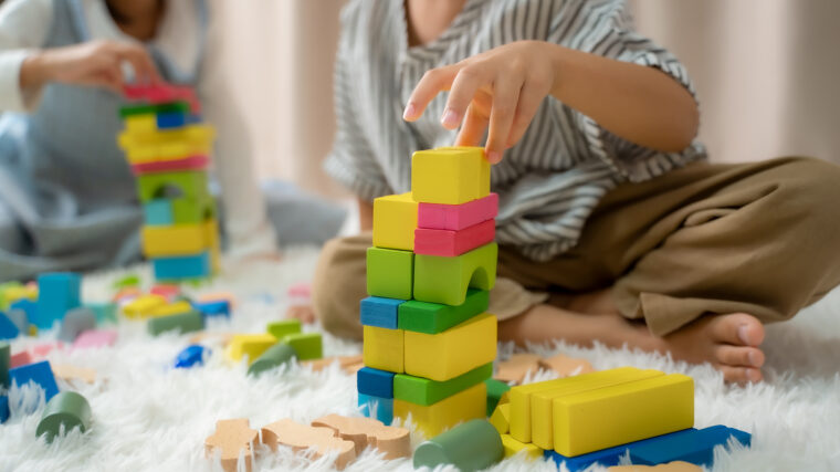 Kaksi lasta leikkimässä palikoilla maton päällä.