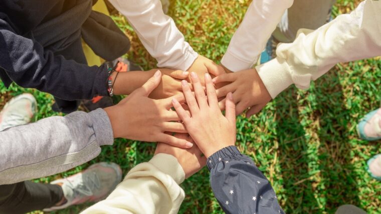 Nuorten kädet yhdessä. Kuvastaa yhteisöllisyyttä.