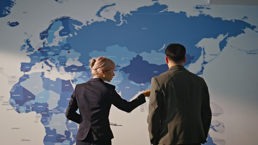 Kartta, jossa näkyy Eurooppa, Afrikka ja Aasia. Kaksi ihmistä seisoo kartan edessä selin kameraan.