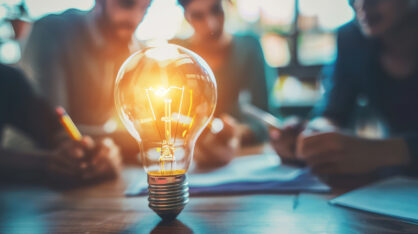 Glowing light bulb on a table with people working in the background.