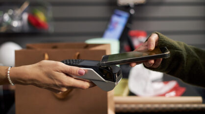 Käsi ojentaa maksupäätettä ja toinen käsi ojentaa puhelinta maksupäätettä kohti.