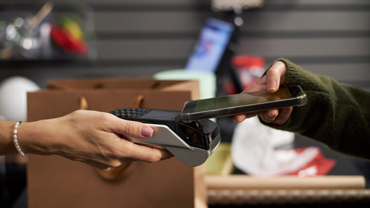 Käsi ojentaa maksupäätettä ja toinen käsi ojentaa puhelinta maksupäätettä kohti.