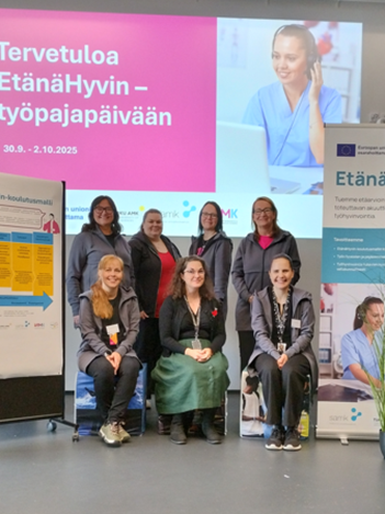 7 naishenkilöä poseeraa kuvassa, taustalla EtänäHyvin markkinointimateriaaleja.