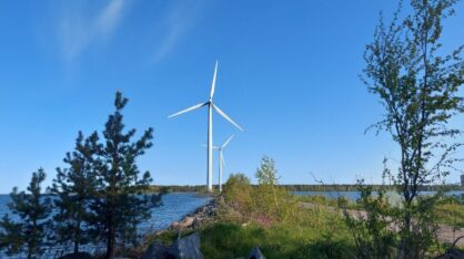 Vesistön tuntumaan sijoittuvia tuulivoimaloita. Sininen taivas, tuulinen päivä.