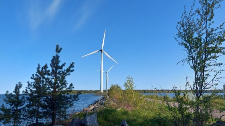 Vesistön tuntumaan sijoittuvia tuulivoimaloita. Sininen taivas, tuulinen päivä.